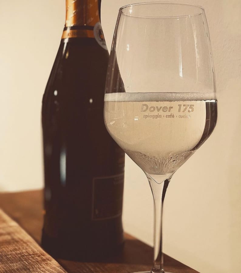 Calice di prosecco con incisione 'Dover 175 spiaggia · cafè · cucina' — aperitivo al Bagno Dover 175